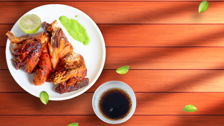 Plate of spicy grilled chicken on wooden table next to cup of Coca-Cola