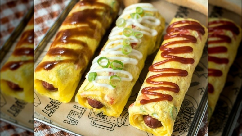 Three Japanese omelets have hot dogs inside them and different drizzles on top