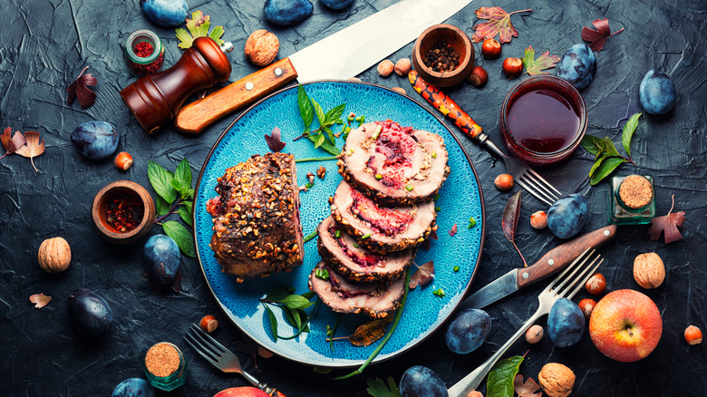 Roast pork with plums and nuts on a table with cutlery and fruits