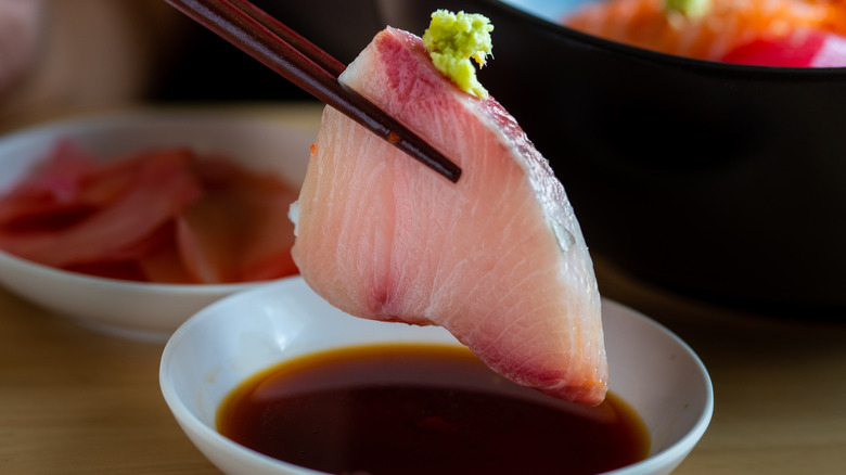 A piece of sashimi with wasabi being dipped in soy sauce