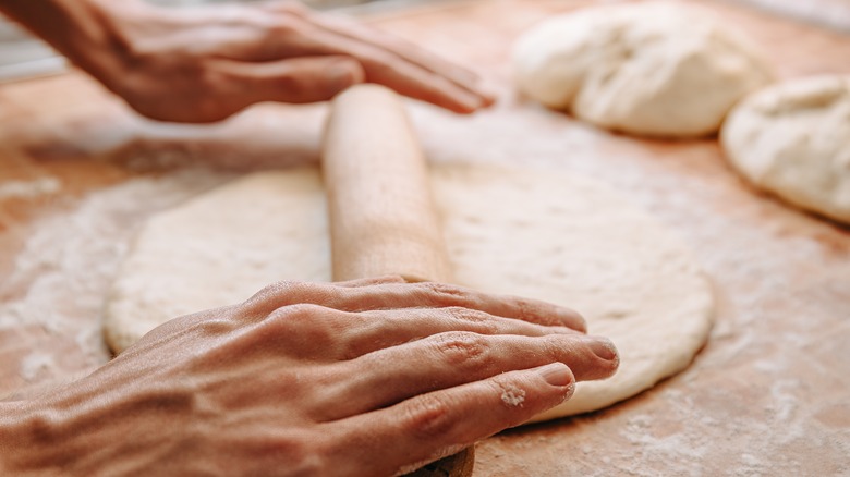 Cooking rolling pizza dough with rolling pin on floured surface