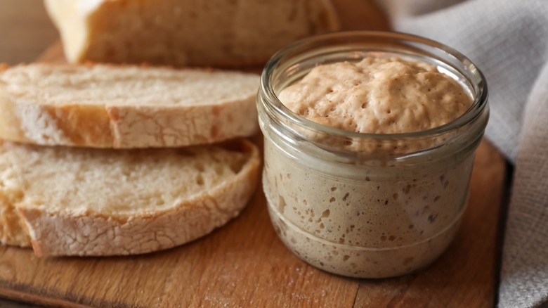 A jar of sourdough starter next to slices of bread