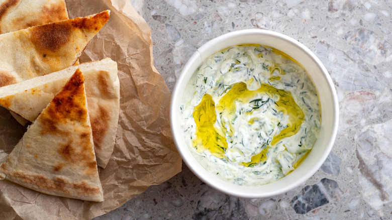 A Greek yogurt dip sits next to several slices of pita bread