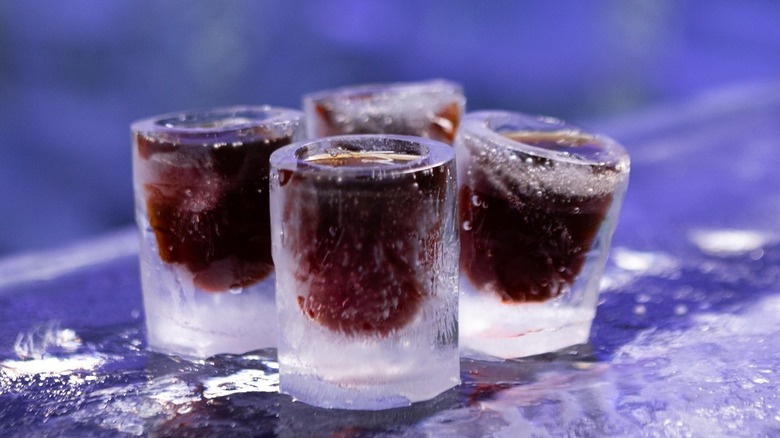 shot glasses made of ice are filled with brown liquor