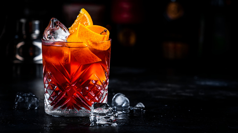 A close up of a Negroni with ice and an orange twist on a black bar.