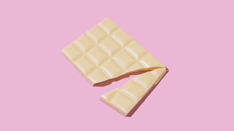 broken bar of white chocolate on pink background