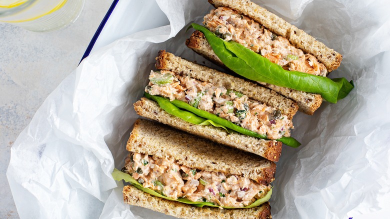 Three halves of a sandwich with tuna salad and lettuce in white paper