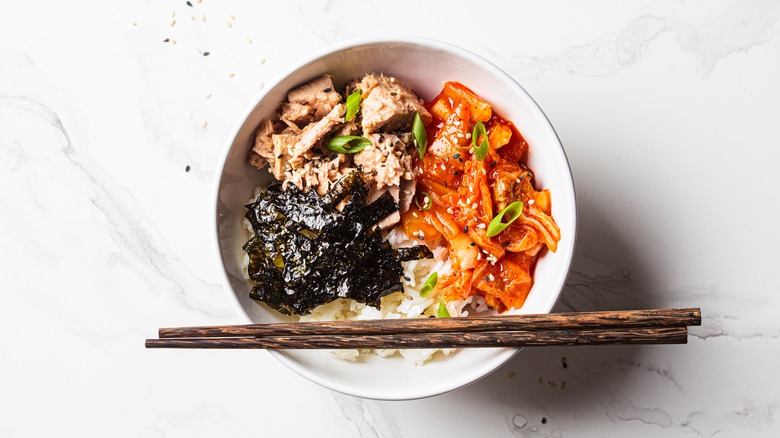 Bowl of kimchi and tuna salad with rice, seaweed, and a pair of chopsticks on the rim