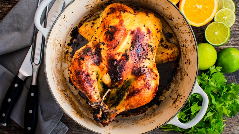 Whole chicken in pot next to serving utensils