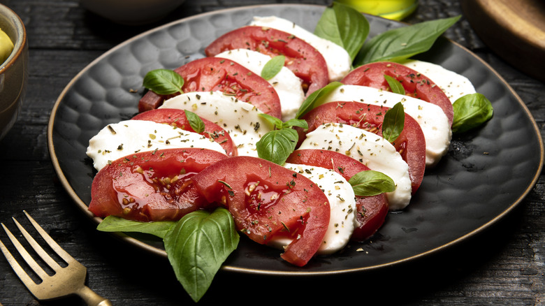 Caprese salad on black plate with tomatoes, mozzarella cheese, basil