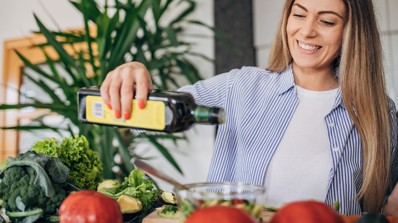 Woman pouring olive oil on veggies
