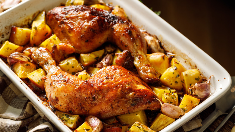 roasted chicken legs in white roasting pan with potatoes