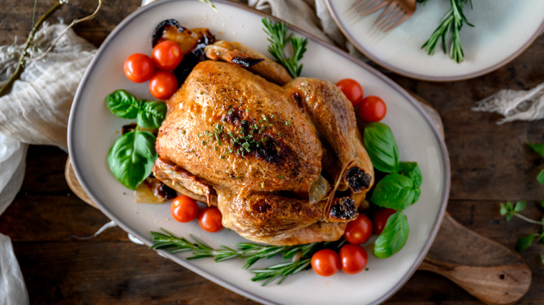 roast chicken dressed with vegetables on white serving dish