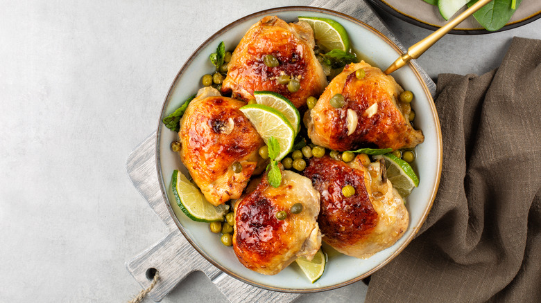 chicken thighs in white serving dish with lime slices and capers