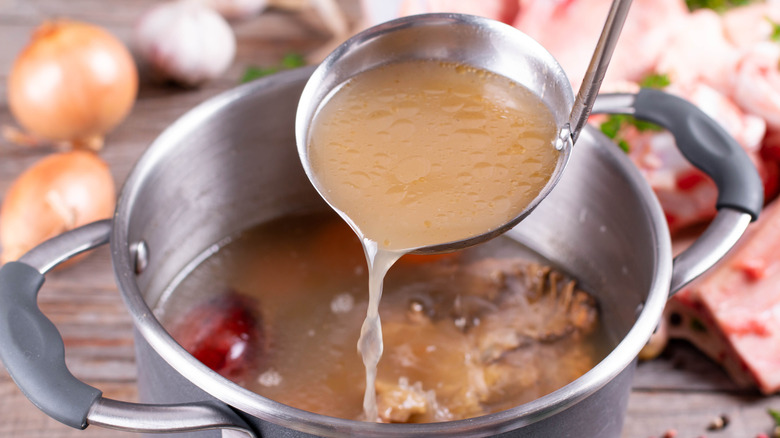 ladle pouring chicken broth into large metal stock pot