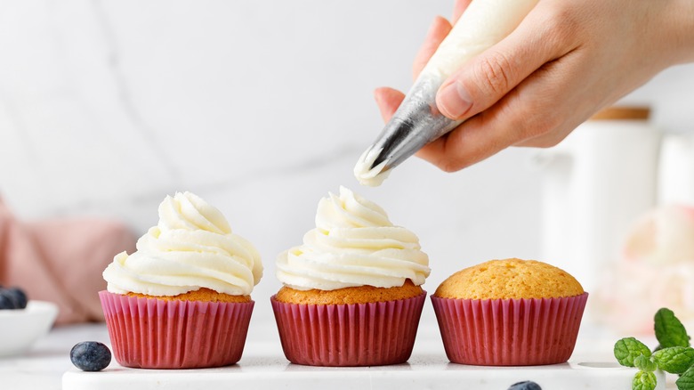 Person decorating cupcakes with frosting