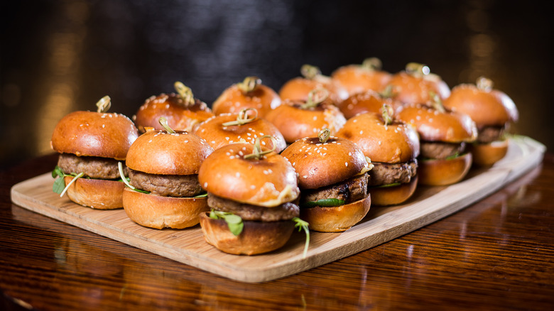 Mini burger sliders on brioche buns on a wooden cutting board