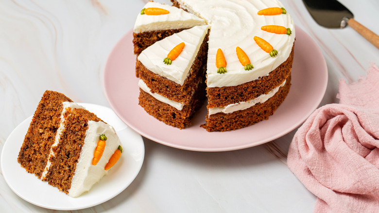 Slice of carrot cake on plate with rest of cake in background