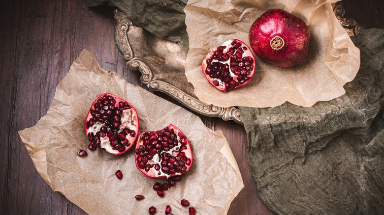 Cut open pomegranates and seeds on brown parchment paper and antique silver tray