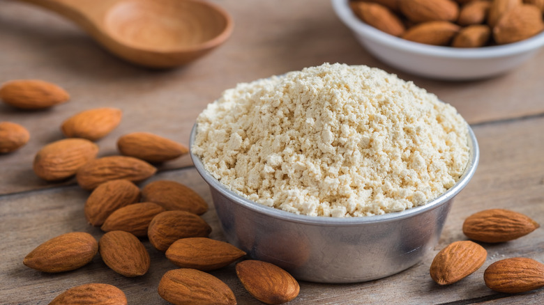 Bowl of almond flour on table surrounded by whole almonds