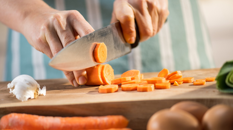 carrots being sliced on a wooden board with a large knife