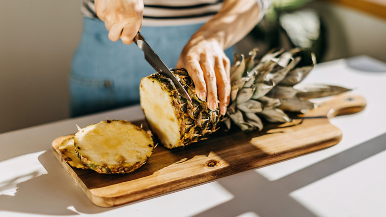 woman slicing pineapple on wooden cutting board