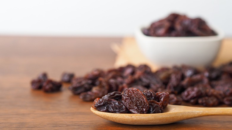 wooden spoon of black raisins with bowl of raisins in background