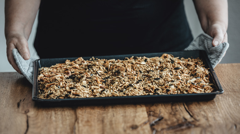 person holding baking tray of toasted oats and nuts