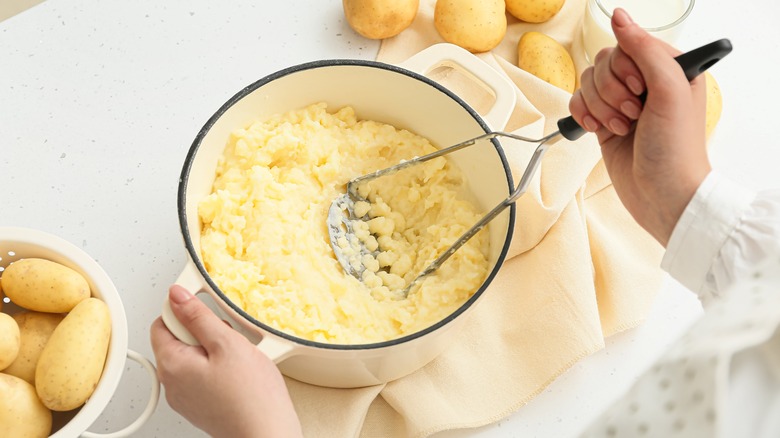hands mashing potatoes in pot
