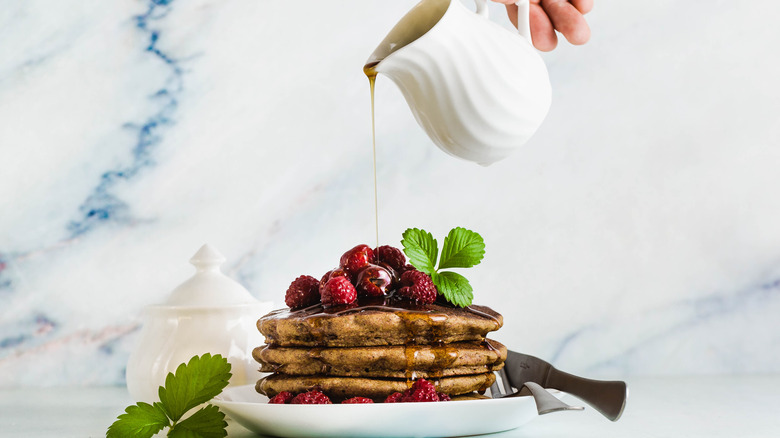 Syrup pouring over buckwheat pancakes and berries