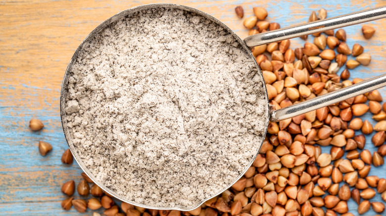 Buckwheat flour in a measuring scoop next to seeds