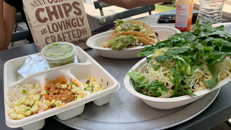 A burrito bowl, two tacos, and sides of guac, corn salsa, and beans on a tray at Chipotle