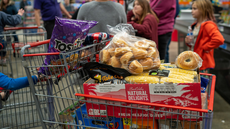 A Costco shopping cart full of groceries is positioned in line at checkout