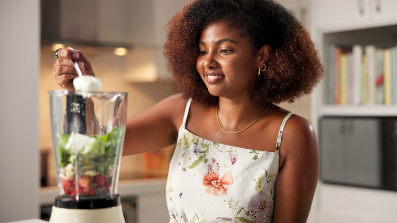 A person adds some fresh yogurt into a blender filled fruits