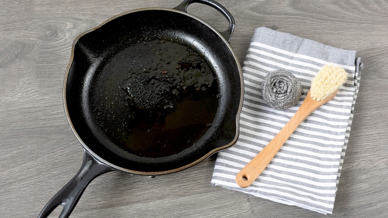 A towel, scrub, and brush next to a cast iron pan