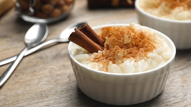 White bowl with rice pudding topped with cinnamon sticks and powdered spice