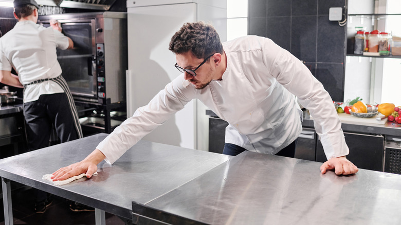 Chef wiping down stainless steel table with cloth in a kitchen