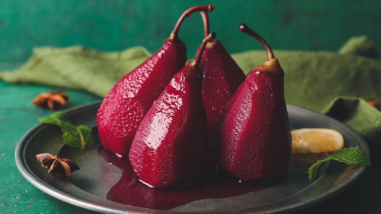 red wine poached pears sit on a plate with mint, star anise, and some citrus