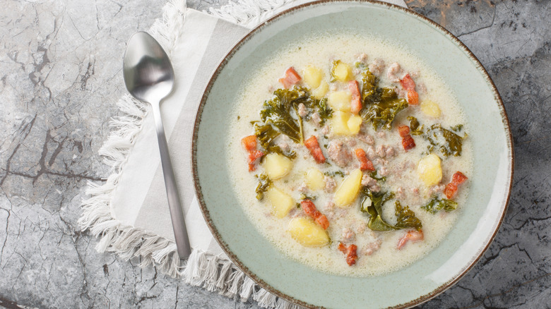 Zuppa Toscana next to a spoon set upon a white cloth placemat with a white marble background