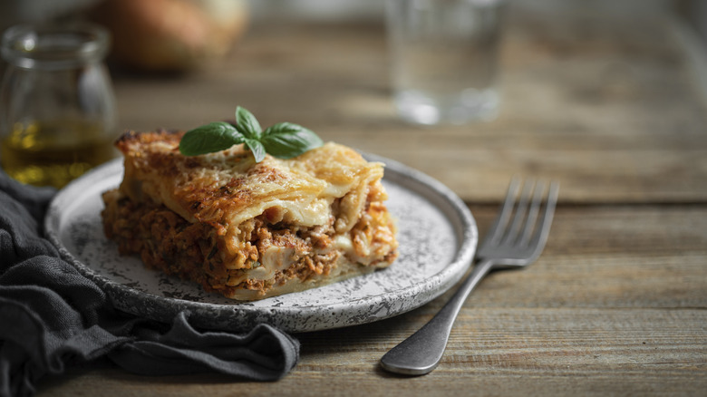 A slice of lasagne sitting on a plate next to fork