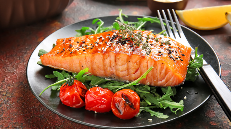 salmon fillet on black plate with greens and blistered cherry tomatoes