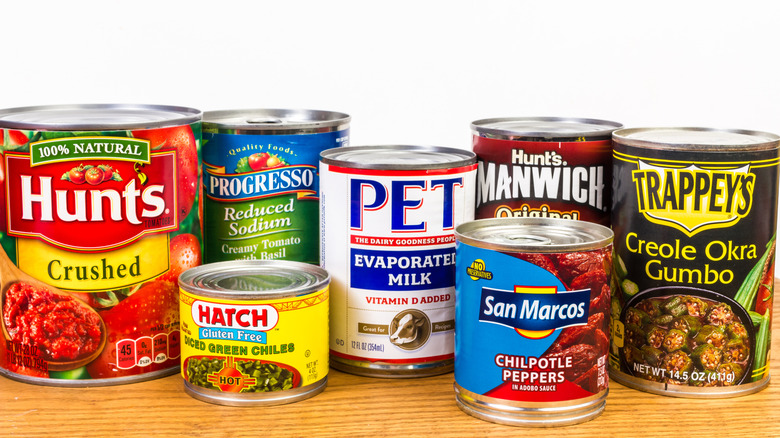 A variety of cans with different foods sit on a wooden surface