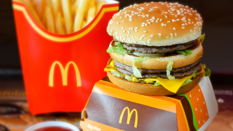 A Big Mac sits on top of a Big Mac box next to a bowl of ketchup and some french fries