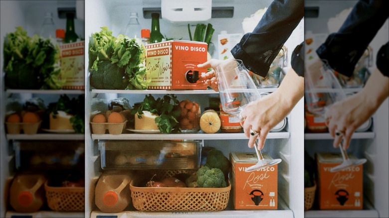 A person reaches for a box of wine in a well-stocked fridge