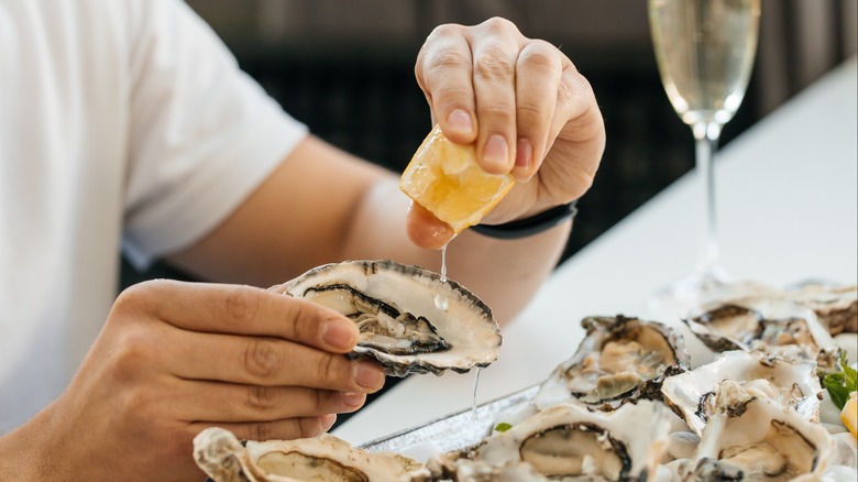 Lemon being squeezed on a shucked oyster