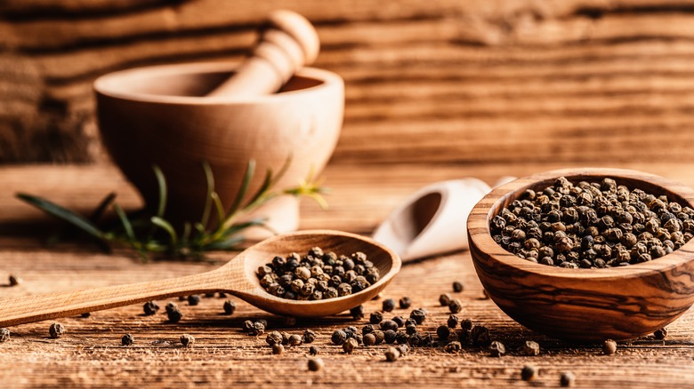 A mortar and pestle next to black peppercorns