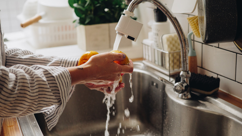 Hands washing citrus under faucet