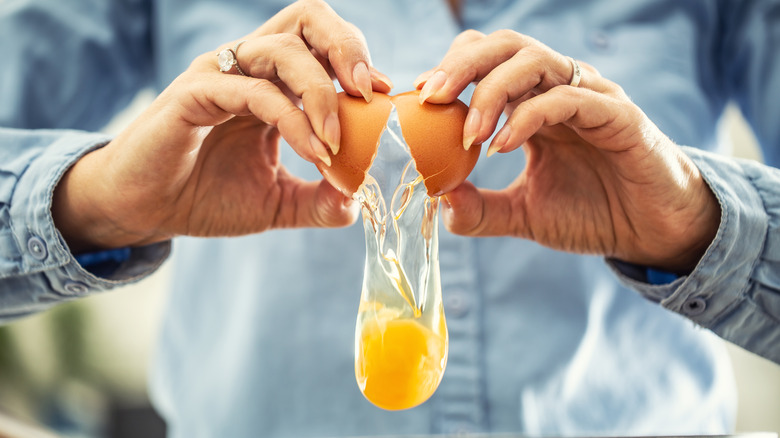 Woman's hands holding a cracked egg with the egg falling out