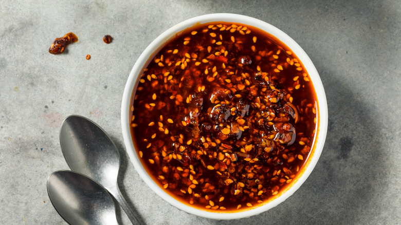 A white bowl of chili crisp oil sits on a marble slab next to two spoons