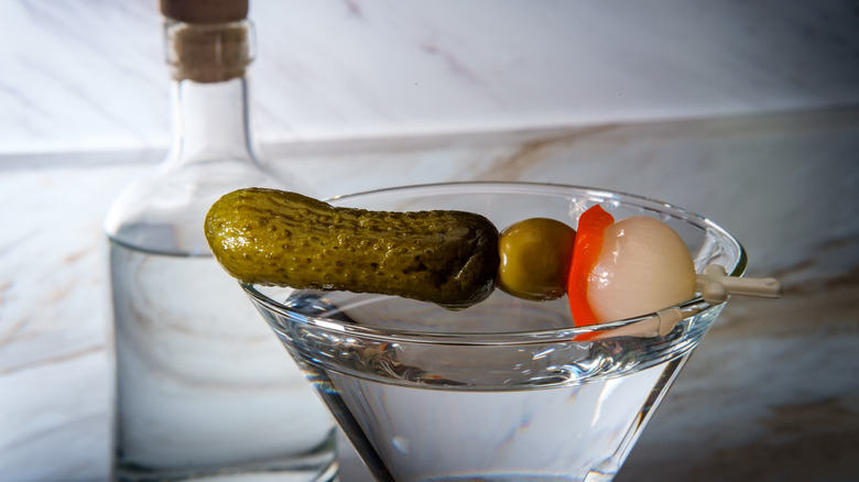 cocktail with pickle garnish and bottle of clear liquor